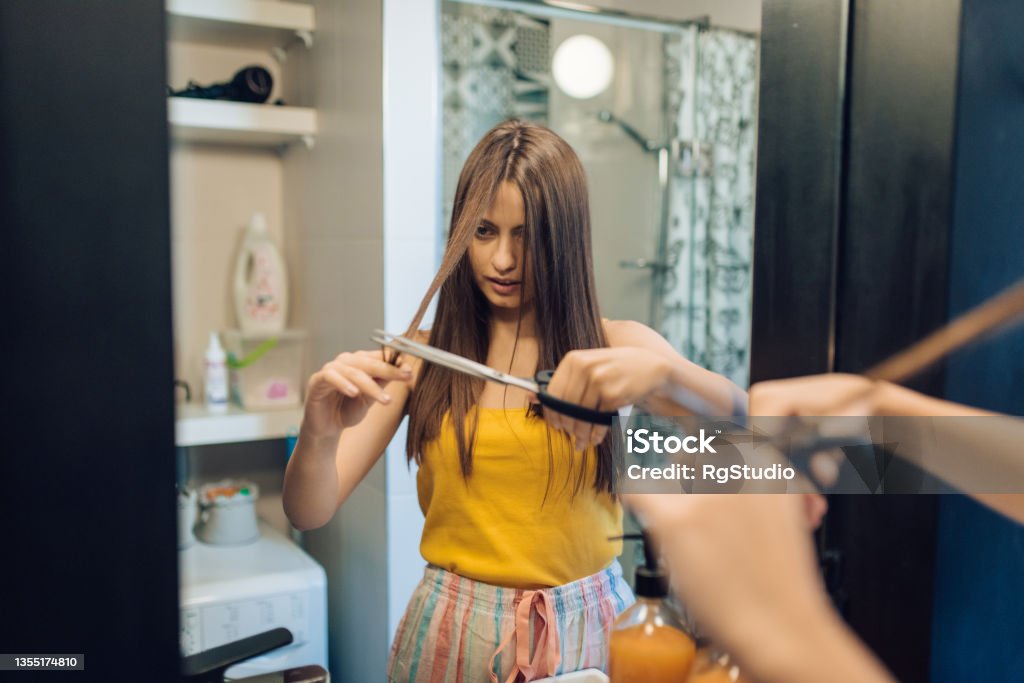 Girl doing herself hairstyle at home Teenage girl doing herself a haircut in the bathroom. Cutting Stock Photo