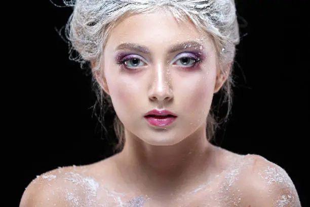 Photo of Winter Beauty Woman in clothes made of frozen flowers covered with frost, with snow on her face and shoulders. Christmas Girl Makeup. Make-up the snow Queen. Isolated on a black background. Close-up