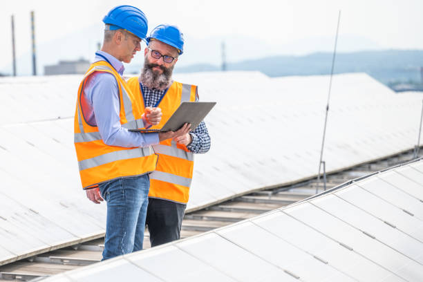 istock Two men using safety equipment standing on flat roof between rows of solar cells and discussing above laptop screen 1355188882