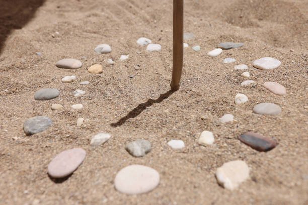 Wooden stick and pebbles on sand showing time by shadow Close-up of wooden stick and pebbles on sand surface showing time by shadow. Rocks sundial on beach. Time to rest. Summer holidays and travelling concept ancient sundial stock pictures, royalty-free photos & images