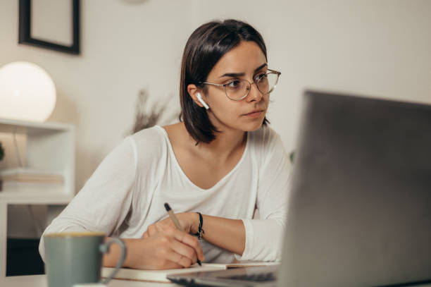 istock Woman writing in a notebook and using a laptop while working from home 1355189715
