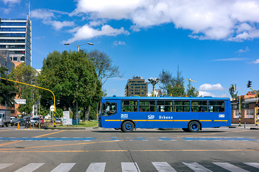 Bogota, Colombia - September 18, 2021: The driver's point of view on the fast lanes of the Westbound carriageway on the Calle 100 or 100 Street, at the point where Carrera 11 cuts across Calle 100 in the Colombian Capital city of Bogota. A blue city public transportation bus is seen crossing the street at the intersection. It is fairly empty. The altitude at street level is 8,660 feet above mean sea level. Horizontal Format; copy space.