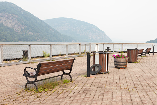 Cold Spring pier along the Hudson River with a view of Storm King Mountain and empty benches during the summer in Cold Spring New York