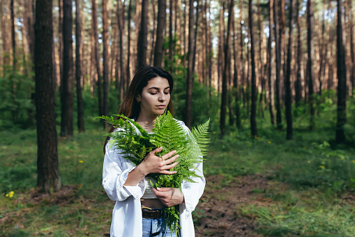 A woman in the woods hugs a bouquet of ferns, a young activist protects the forest