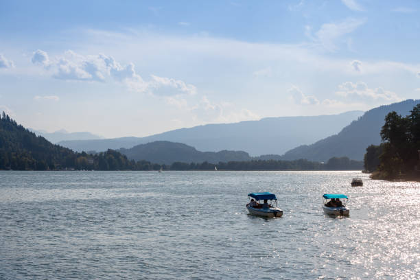 two electric mini boats on ossiacher see lake in summer. Ossiachersee, or Ossiach lake, is an alpine see near Villach, in Carinthia. "n"nPicture of two touristic boats, electric, cruising on ossiacher see lake in Sattendorf, Austria. Lake Ossiach is a lake in the Austrian state of Carinthia. It is the state's third largest lake, superseded only by Lake Wörth and Lake Millstatt. villach stock pictures, royalty-free photos & images