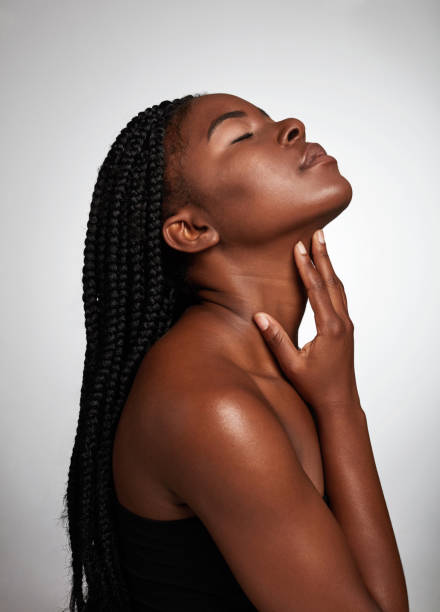 studio shot of an attractive young woman posing against a grey background - touching neck imagens e fotografias de stock