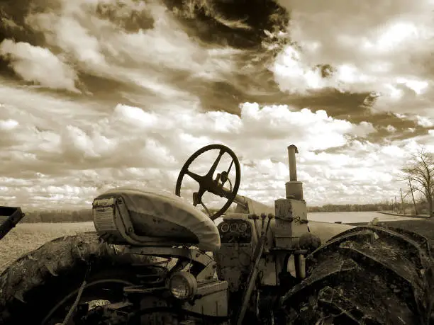 An old farm tractor in front of a dramatic cloud-filled sky. Imaged in infrared light.