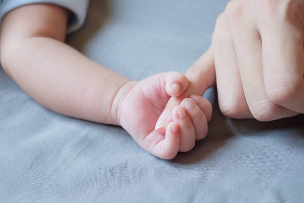 istock Baby hand with mother finger on bed 1355201545