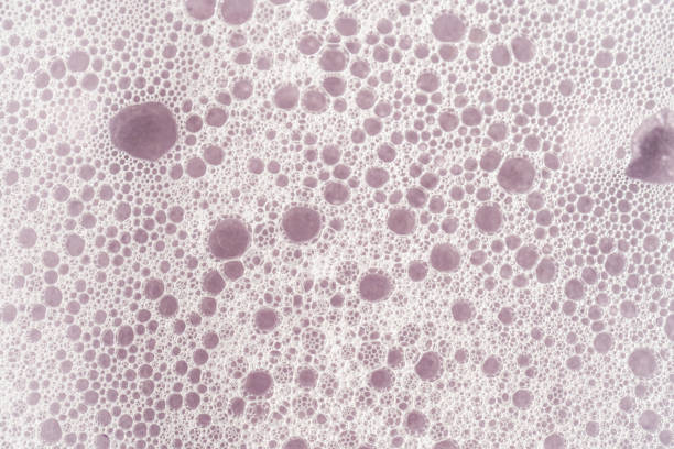 Texture of white foam on a purple background. The texture can be useful for demonstrating soap, shampoo, detergent.