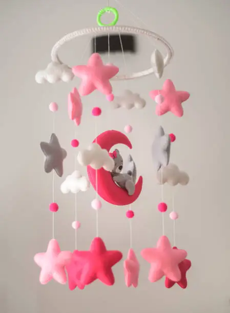 Baby crib hangings, Felt cot mobile with soft plushie stars clouds and moon with sleeping teddy, Cot isolated against a neutral color background. Beautiful music toy over the crib in the baby room.