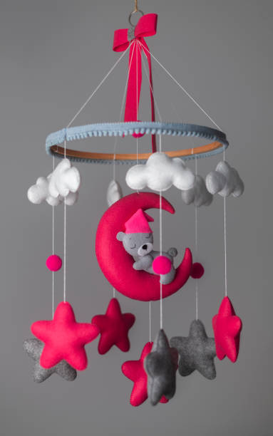 baby crib hangings, felt cot mobile with stuffed soft stars clouds and moon with sleeping teddy, cot isolated against neutral grey color background. a cute teddy wearing a pink hat. baby room decor. - using mobile imagens e fotografias de stock
