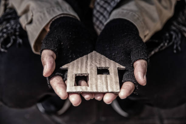 House shaped cardboard on dirty hands of homeless beggar. stock photo
