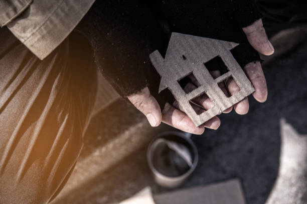 House shaped cardboard on dirty hands of homeless beggar. stock photo