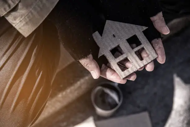 Photo of House shaped cardboard on dirty hands of homeless beggar.