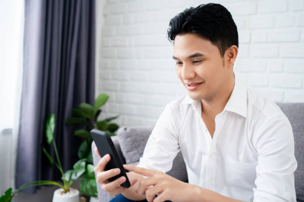 istock Relaxed man sitting on couch at home using smartphone. 1355216397