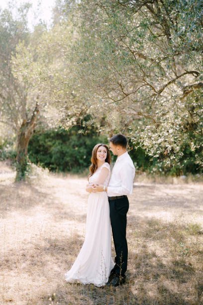 istock Groom hugs bride from behind while standing in the olive grove 1355216578