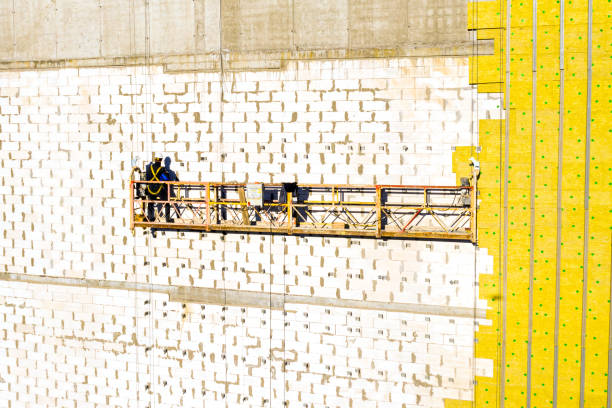 istock Professional construction Worker on scaffold elevator insulated wall facade with mineral wool. roofers wearing safety harness insulating wall facade at height on new building in crane 1355217687