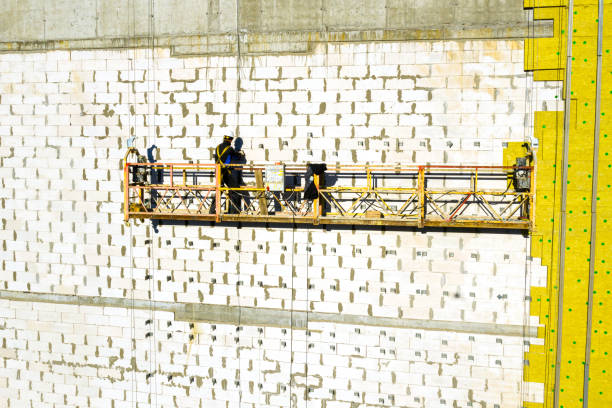 istock Professional construction Worker on scaffold elevator insulated wall facade with mineral wool. roofers wearing safety harness insulating wall facade at height on new building in crane 1355218517