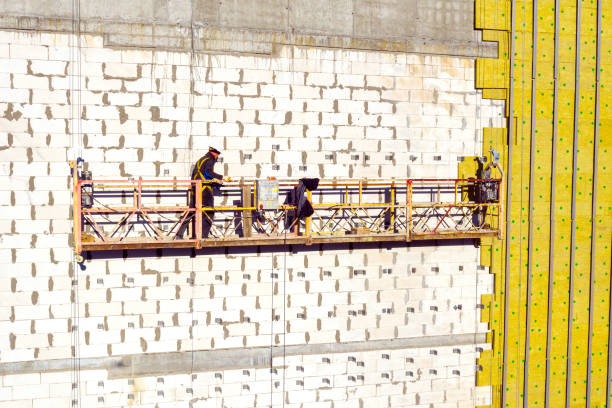 istock Professional construction Worker on scaffold elevator insulated wall facade with mineral wool. roofers wearing safety harness insulating wall facade at height on new building in crane 1355219137