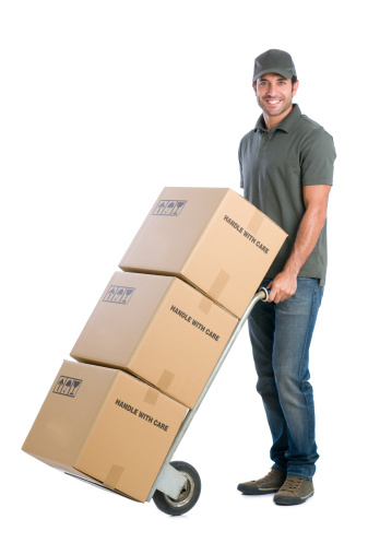 Smiling young delivery man moving boxes with dolly, isolated on white background.