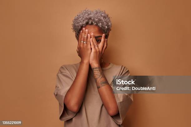 Frightened Dark Skinned Woman Covers Face With Palms Peeks Through Fingers Stock Photo - Download Image Now