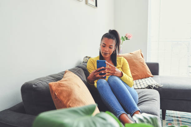 istock Shot of a young woman using a cellphone while relaxing on a sofa at home 1355221043