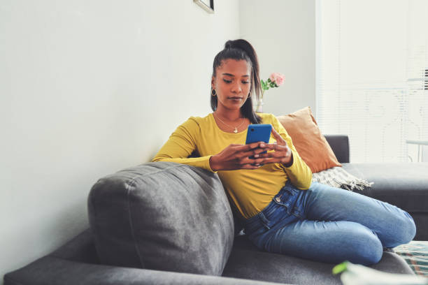 istock Shot of a young woman using a cellphone while relaxing on a sofa at home 1355221064