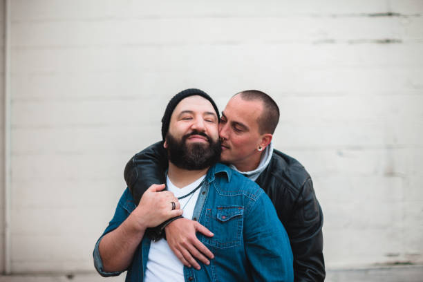 Two Affectionate Men in Love Portrait of a mixed race gay couple in the city together showing affection. Shot against a brick wall with room for copy space. The men are in their 30s and 40s. gay man stock pictures, royalty-free photos & images