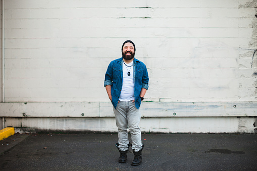 A fashionable bearded mixed race man smiling in the city. Shot against a wall giving room for copy space.