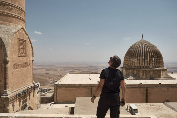 Man on roof looks to minaret Young adult man stands on roof and looks to ancient minaret. Mesopotamian plain and Grand Mosque dome at background. Man opposite middle-eastern landscape. Mardin, Turkey ulu camii stock pictures, royalty-free photos & images