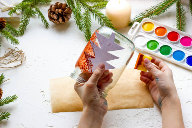 istock the boy's hands make a candlestick from a glass jar painted with red paint with a silhouette of a Christmas tree, step by step instructions, step 4 1355226794