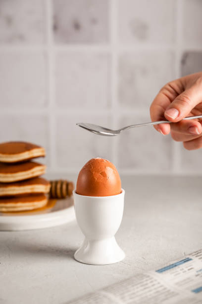 istock A woman's hand breaks eggshells with a spoon for breakfast in the white kitchen at home 1355226838