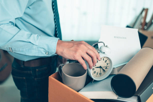 i disoccupati raccolgono la sveglia nella scatola di cartone e nella tazza di caffè, nella calcolatrice e nel tubo di disegno nella scatola. lasciare un lavoro, un uomo d'affari licenziato o lasciare un lavoro concpet. - unemployment benefits rejection application form foto e immagini stock