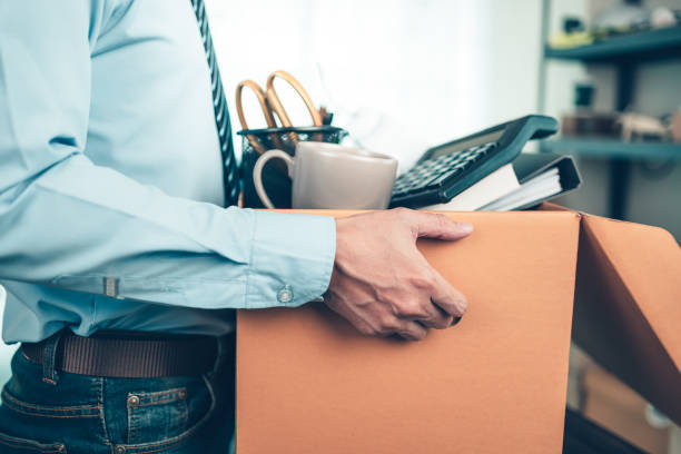 Unemployed hold cardboard box and resignation letter, dossier, alam clock, coffee cup, calculator and drawing tube in box. Quiting a job, businessman fired or leave a job concpet. stock photo