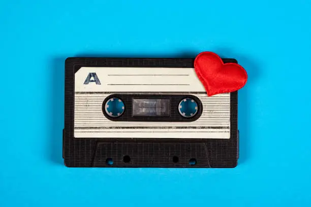 Old Audio Cassette with a Red Heart on the Blue Paper Background closeup