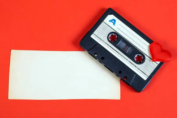 Old Audio Cassette with a Heart Shape and Blank Paper on the Red Background closeup