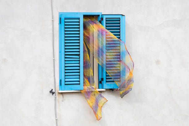 Italy. Scauri. Curtains are pulled out of the open window through the shutters.
