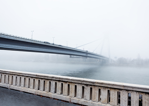 Balustrade and bridge over Danube . Fog over the river in the morning . Riverside sidewalk with balustrade