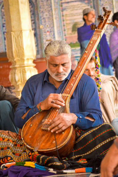 Jodhpur, Rajasthan, India - 26th Dec 2023: Rajasthani Indian musician sitting cross legged in colorful turban and white kurta pyjama local clothing in front of a brick wall at a mahal palace