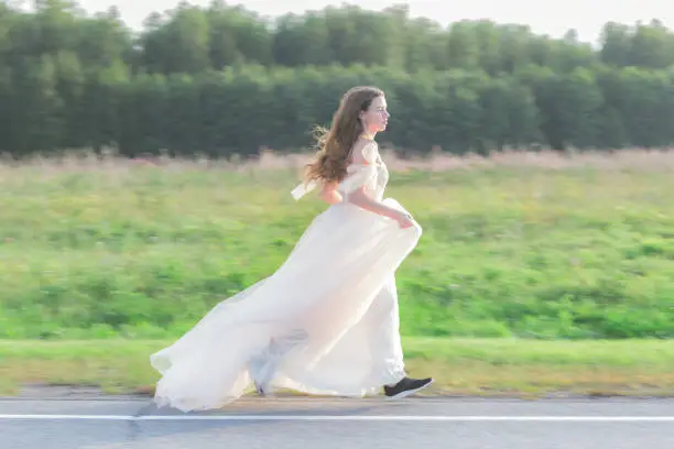 Bride in a white dress runs down the road