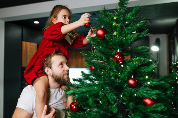 크리스마스 트리를 장식하는 아빠의 어깨에 앉아있는 귀여운 어린 소녀 - spherical joint 뉴스 사진 이미지
