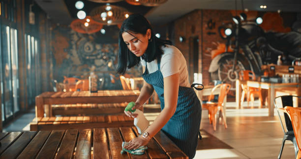снимок молодой женщины, дезинфицирующей столы во время работы в ресторане - waiter стоковые фото и изображения