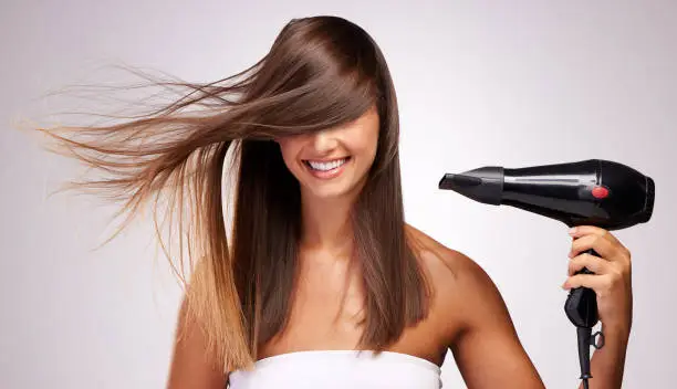 Photo of Studio shot of an attractive young woman blowdrying her hair against a grey background