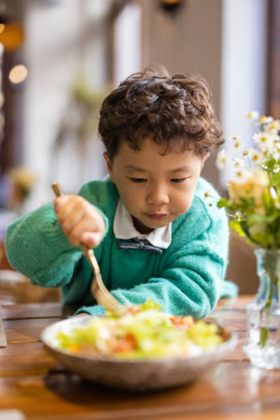 istock little boy eating salad in a restaurant 1355243629