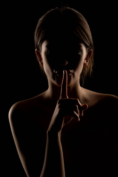 a young teenage girl puts her finger to her lips secrecy don't tell anyone sharply turn around look into the frame wave a finger negatively. on a white background stern look