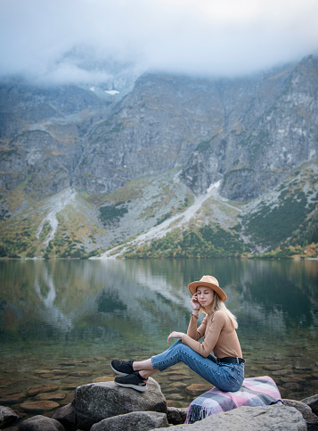 Young woman tourist sitting on the mountain peak and beautiful mountains. Landscape with sporty girl, green forest, hills , sky, lake. Travel and tourism.