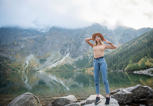 Young tourist girl in a hat with hands up on the top of the mountains admires the nature