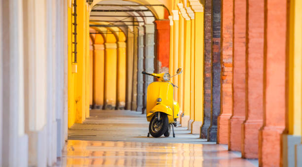 This is a very old yellow italian scooter parked under Modena colorful arcades. Modena, Emilia Romagna, Italy.