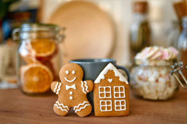 Merry Christmas and Happy New Year! Close-up of gingerbread spices in the shape of a man and a small house. In the background are jars of marshmallows and dried orange slices.