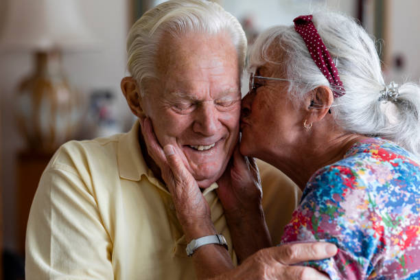 I Love You Forever Senior couple at home in the North East of England. The wife is kissing her husband's cheek while he laughs with his eyes closed. 80 89 years stock pictures, royalty-free photos & images